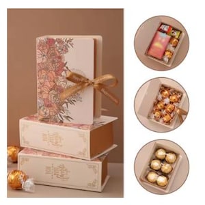 May include: Gift boxes stacked, featuring a floral design and a gold ribbon. The top box has a book-like shape. The boxes are filled with chocolates. The boxes are beige with gold accents. The ribbon says "Happy Moments".