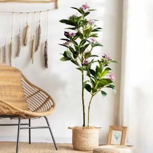 May include: Artificial plant with green leaves and pink flowers in a woven basket. The plant is tall and has a natural look.