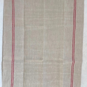May include: A rectangular piece of natural beige linen fabric featuring a woven texture. The textile is decorated with two vertical stripes, each consisting of a thick red line flanked by two thinner red lines, positioned near the left and right edges.