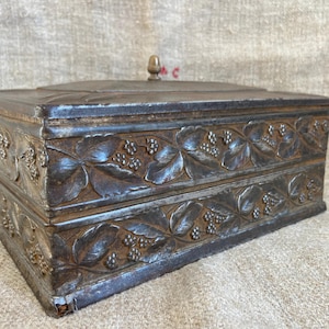 May include: A vintage metal box with a floral design. The box has a hinged lid with a small knob on top. The box is made of a dark metal with a slightly worn finish.
