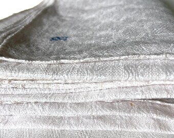 May include: A stack of folded white linen towels. The towels have a textured weave and a soft, slightly worn appearance. A small blue detail is visible on the top towel.