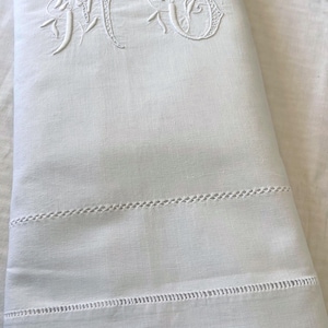 May include: White linen sheet with embroidered initials "MC" in a floral design. The sheet features decorative stitching along the bottom edge. A classic and elegant bedding item.