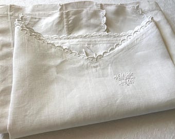 Op de afbeelding: Off-white linnen beddengoedset, met een kussensloop met geschulpte rand en geborduurd monogram. De set bevat een opgevouwen laken, dat de textuur en het ontwerp van de stof laat zien. Een klassiek, vintage-geïnspireerd textiel.