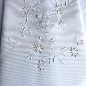 Puede incluir: Tejido blanco a rayas con diseño floral e inicial bordado. El bordado presenta las letras "JP" entrelazadas con delicadas flores y hojas. La tela tiene una apariencia sutil y texturizada.