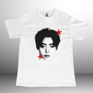 Könnte beinhalten: Ein weißes Kurzarm-T-Shirt mit einem schwarz-weißen Halbton-Porträt einer Person mit dunklem Haar. Die Grafik enthält zwei leuchtend rote fünfzackige Sterne, die sich oben rechts und unten links neben dem Gesicht befinden.