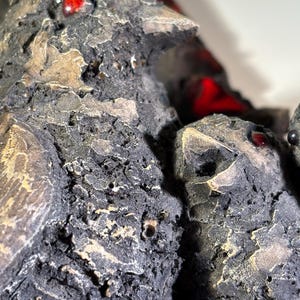 May include: Close-up of a ceramic bird sculpture with a textured, rough surface. The bird has red glass eyes and is painted in shades of brown and gray.