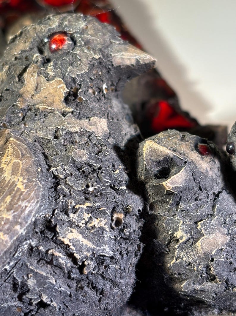 May include: Close-up of a ceramic bird sculpture with a textured, rough surface. The bird has red glass eyes and is painted in shades of brown and gray.