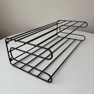 Op de afbeelding: Zwart metalen draadrek met een rechthoekige vorm. Het rek heeft meerdere horizontale staven en afgeronde randen. Ontworpen voor opslag en organisatie, geschikt voor diverse items.