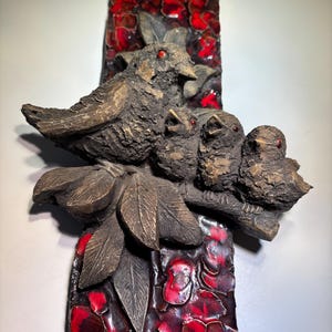 May include: A ceramic wall sculpture featuring a family of birds perched on a branch with red floral background.