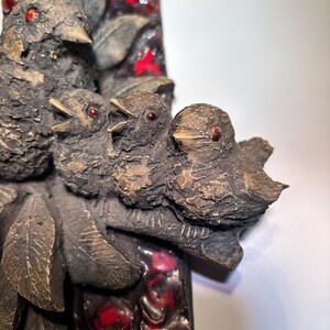 May include: A ceramic wall art piece featuring a group of four birds perched on a branch. The birds are brown with red eyes and are set against a background of red and black mosaic tiles.
