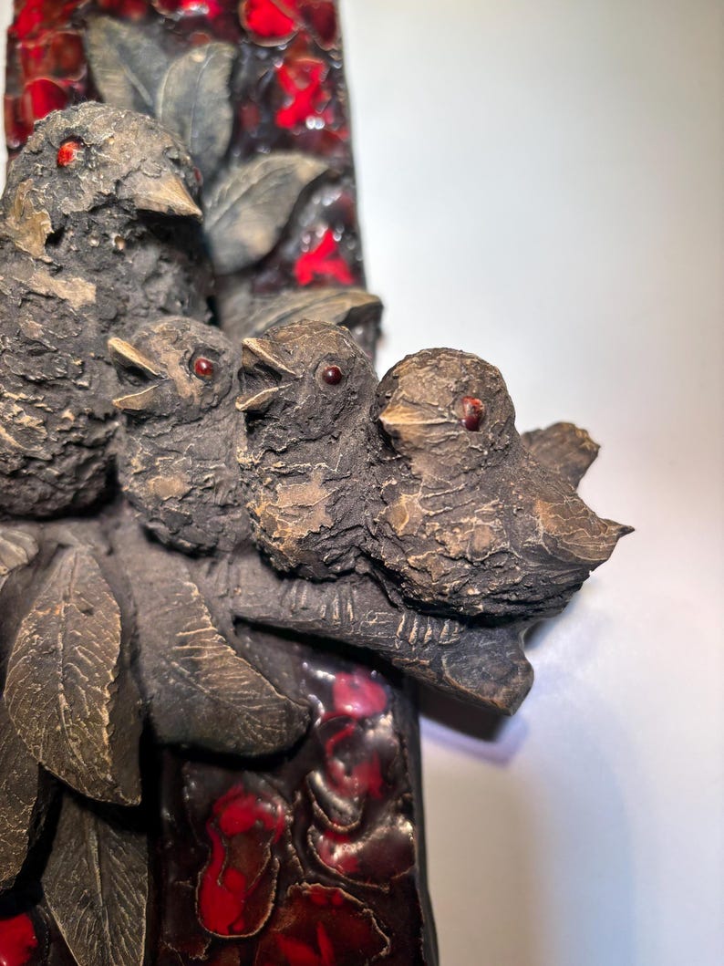 May include: A ceramic wall art piece featuring a group of four birds perched on a branch. The birds are brown with red eyes and are set against a background of red and black mosaic tiles.