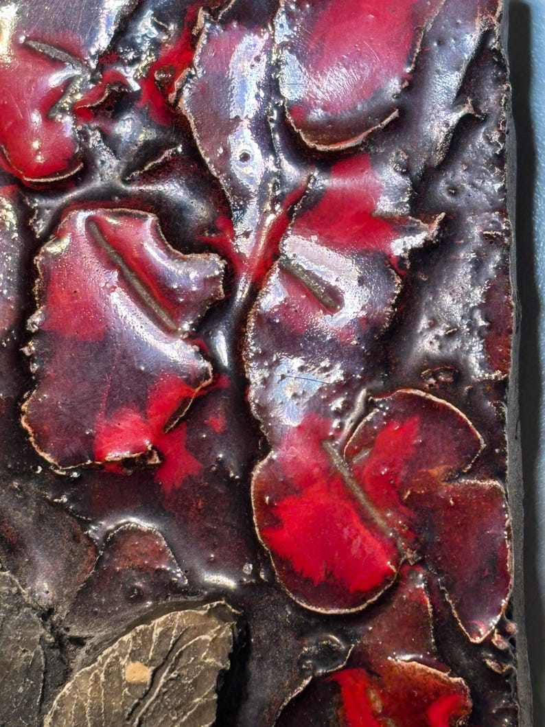 May include: Close-up of a ceramic tile with a textured surface. The tile is decorated with a red and black glaze, creating a abstract pattern.