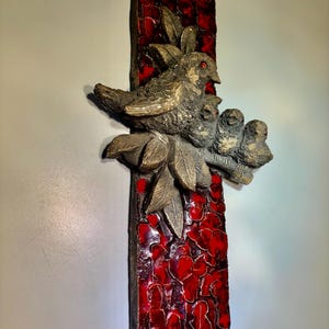 May include: A ceramic wall sculpture featuring three birds perched on a branch with leaves. The background is a mosaic of red tiles.