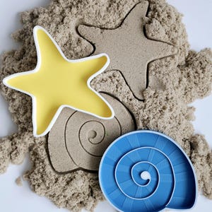 Pode incluir: Três moldes de areia para brincar na areia. Uma estrela do mar amarela, uma concha marrom e uma concha azul.
