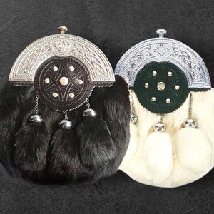 Puede incluir: Dos sporrans escoceses, uno negro y otro blanco, con detalles metálicos plateados. Cada sporran presenta un cuerpo de piel, una parte superior decorativa de metal y tres borlas colgantes con adornos metálicos plateados.