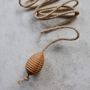 May include: A cat toy made from natural fibres, featuring a wooden, egg-shaped end with horizontal grooves. The toy is attached to a long, twisted rope with a knot at the end. The rope and wooden end are light brown.