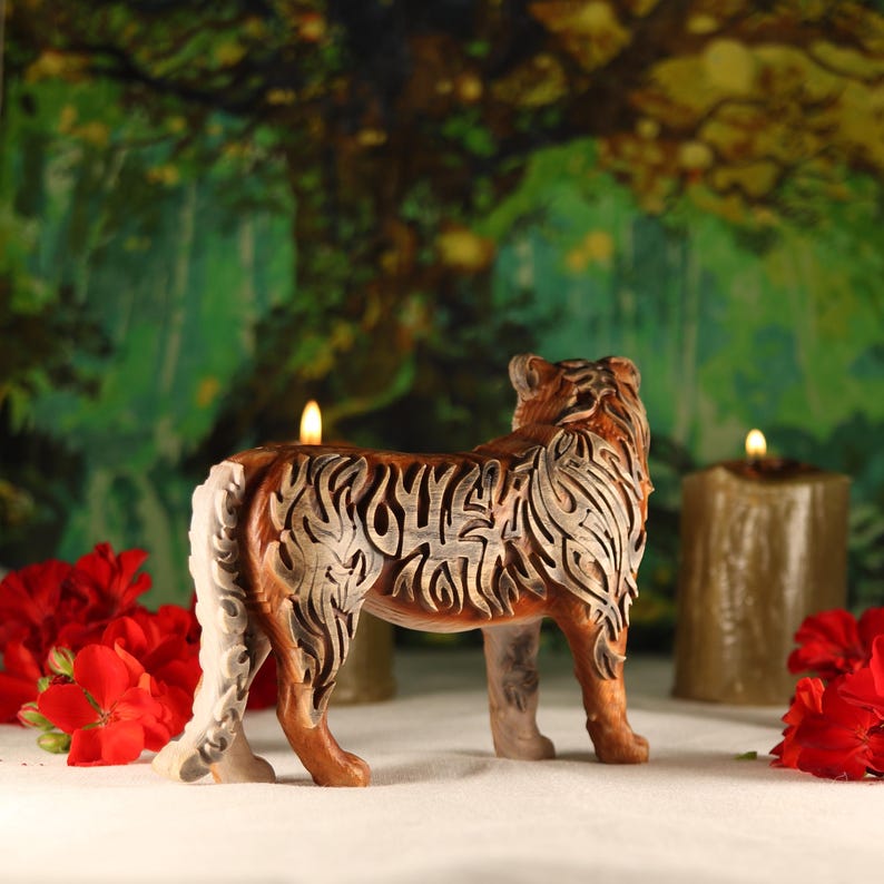 May include: A wooden carved tiger figurine with intricate details, standing on a white surface with red flowers and candles in the background.