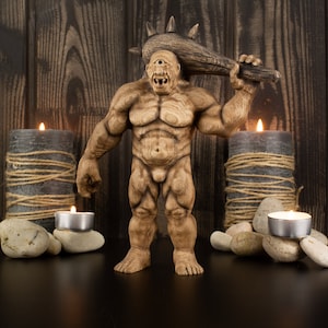 May include: A wooden figurine of a cyclops monster holding a spiked club. The figurine is standing on a wooden surface with candles and rocks around it.