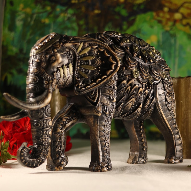 May include: A decorative elephant figurine with intricate details. The elephant is made of a dark brown material and has gold accents. The elephant is standing on all four legs and has its trunk raised.