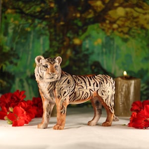 May include: A detailed ceramic tiger figurine with intricate brown and white markings. The tiger is standing on a white surface with red flowers in the background.