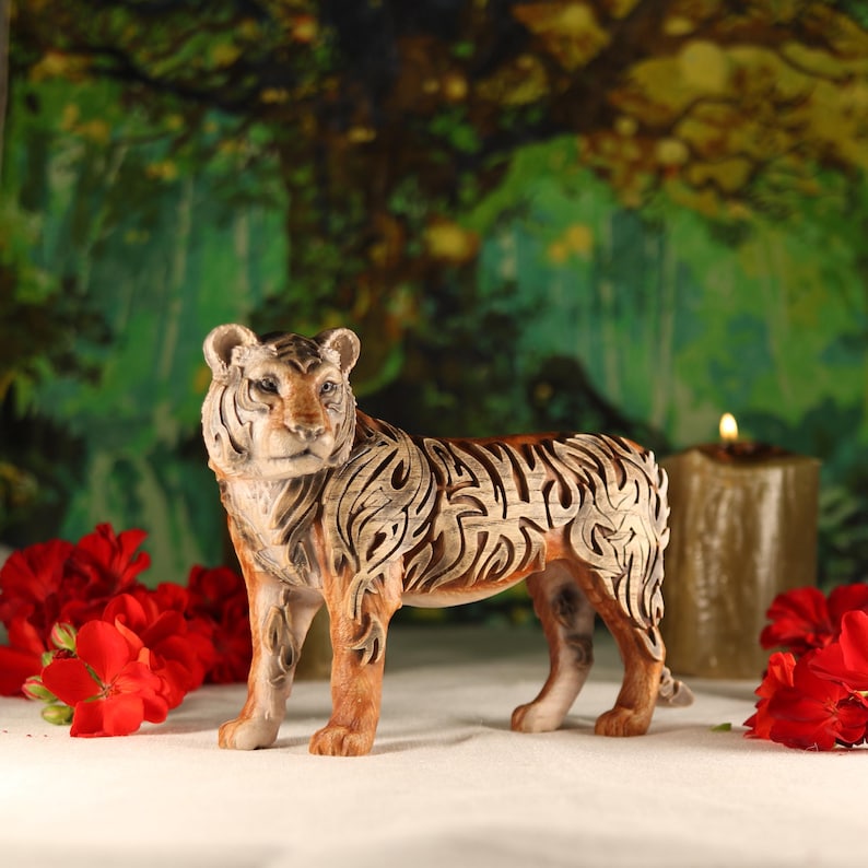 May include: A detailed ceramic tiger figurine with intricate brown and white markings. The tiger is standing on a white surface with red flowers in the background.