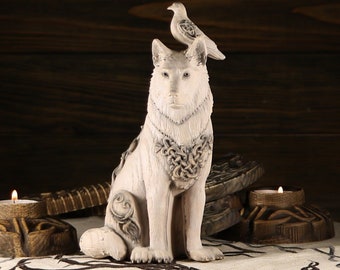 May include: White ceramic figurine of a wolf with a bird perched on its head. The wolf is wearing a Celtic knot necklace and has intricate details on its fur. The figurine is sitting on a wooden surface.