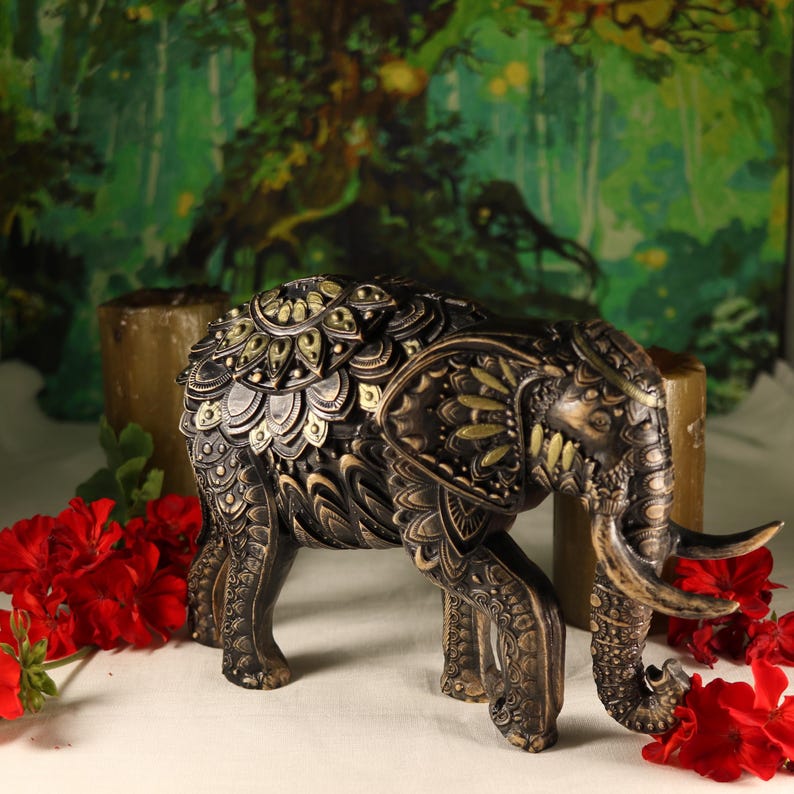 May include: A black and gold decorative elephant figurine with intricate details. The elephant is standing on a white surface with red flowers in the background.