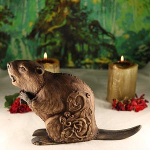 May include: A brown wooden beaver figurine with intricate carvings on its back. The beaver is sitting on its haunches with its tail extended behind it. The figurine is set against a backdrop of a green and brown forest scene.