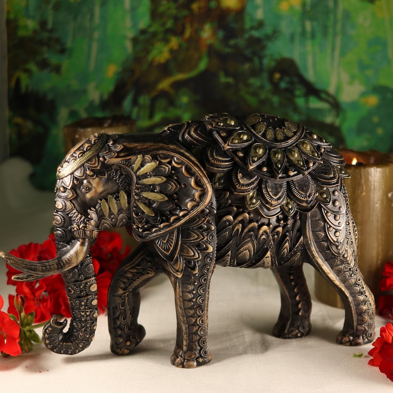 May include: A black and gold elephant figurine with intricate carvings and green gemstone accents. The elephant is standing on a white surface.