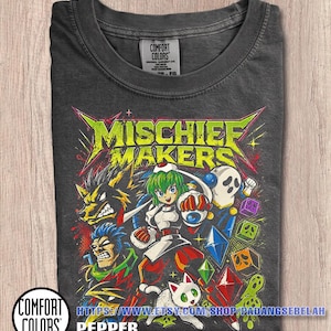 May include: A charcoal gray t-shirt featuring a graphic print with the text MISCHIEF MAKERS in lime green. The design includes a central character with green hair, a wolf-like creature, a skull-faced figure, and a white cat, surrounded by colorful geometric shapes and crystals.