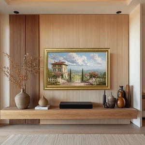 May include: A framed landscape painting with a gold frame hangs on a light wood paneled wall. A wooden shelf below holds decorative vases, a black soundbar, and a small book. A large vase with dried branches sits to the left.