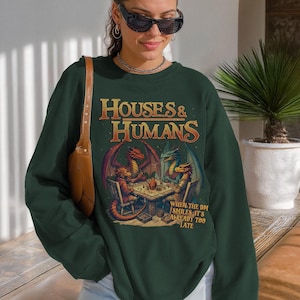 May include: Forest green sweatshirt with the text "HOUSES & HUMANS" and a graphic of dragons playing a board game. The graphic includes the text "WHEN THE DM SMILES IT'S ALREADY TOO LATE".