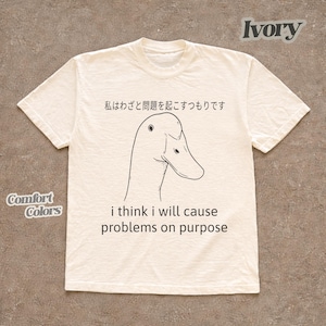May include: Ivory-colored t-shirt with a black line drawing of a duck and the phrase "i think i will cause problems on purpose." Japanese text is above the duck graphic. The shirt is labeled "Comfort Colors."