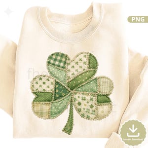 May include: Cream-colored sweatshirt featuring a large, patchwork shamrock design in various shades of green. The shamrock is made of different fabric patterns, including gingham and floral prints. The design is centered on the front of the sweatshirt.