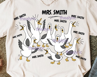 May include: White t-shirt featuring a cartoon illustration of geese with the text "MRS. SMITH" above them and around the geese. The geese are in various poses, with some honking.