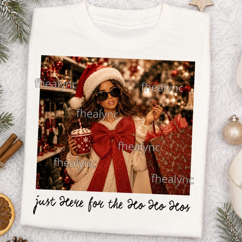 May include: A white t-shirt featuring a graphic print of a person wearing a red and white Santa hat, black sunglasses, and a cream-colored sweater with a large red bow. The person holds a red cup and a red gift bag. Text reads: just here for the Ho Ho Hos.