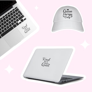 May include: Two white laptop computers with black text stickers. One sticker says "Kind but not quiet" and the other says "Queen Energy Only" with a crown above the text. A white baseball cap with a black sticker that says "Queen Energy Only" with a crown above the text.