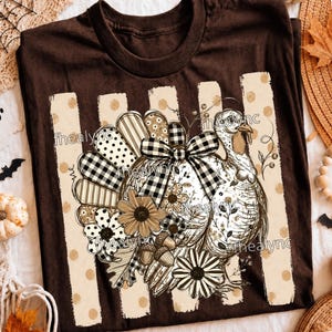 May include: A dark brown t-shirt featuring a graphic of a turkey with a black and white buffalo plaid bow. The turkey is surrounded by flowers, acorns, and leaves, set against a background of vertical beige stripes with brown polka dots.