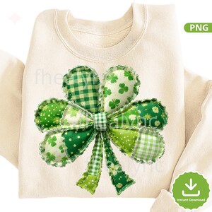 May include: A cream-coloured sweatshirt featuring a large, appliquéd shamrock design. The shamrock is made from various green fabrics, including polka dots, gingham, and floral patterns. The design is centred on the front of the folded sweatshirt.