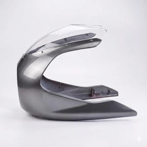 May include: A motorcycle fairing in a metallic gray finish with a clear windshield. The fairing has a curved design and is made of a durable material. The windshield is attached with small screws.