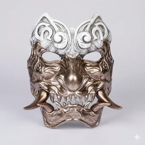 Peut inclure: Un masque détaillé à deux tons avec un design démoniaque. La partie supérieure est blanche avec des motifs tourbillonnants, tandis que la moitié inférieure est de couleur bronze, avec des dents acérées et des cornes incurvées. Le masque est probablement destiné à un costume ou à la décoration.