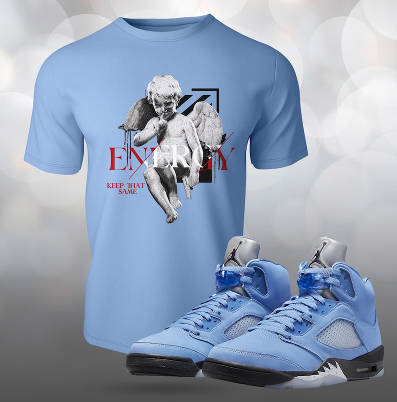 Pu&ograve; includere: Maglietta blu chiaro con una grafica di un angelo con le ali e la parola "ENERGY" con il testo "KEEP THAT SAME" sotto. Un paio di scarpe Air Jordan 5 Retro blu chiaro con accenti neri.