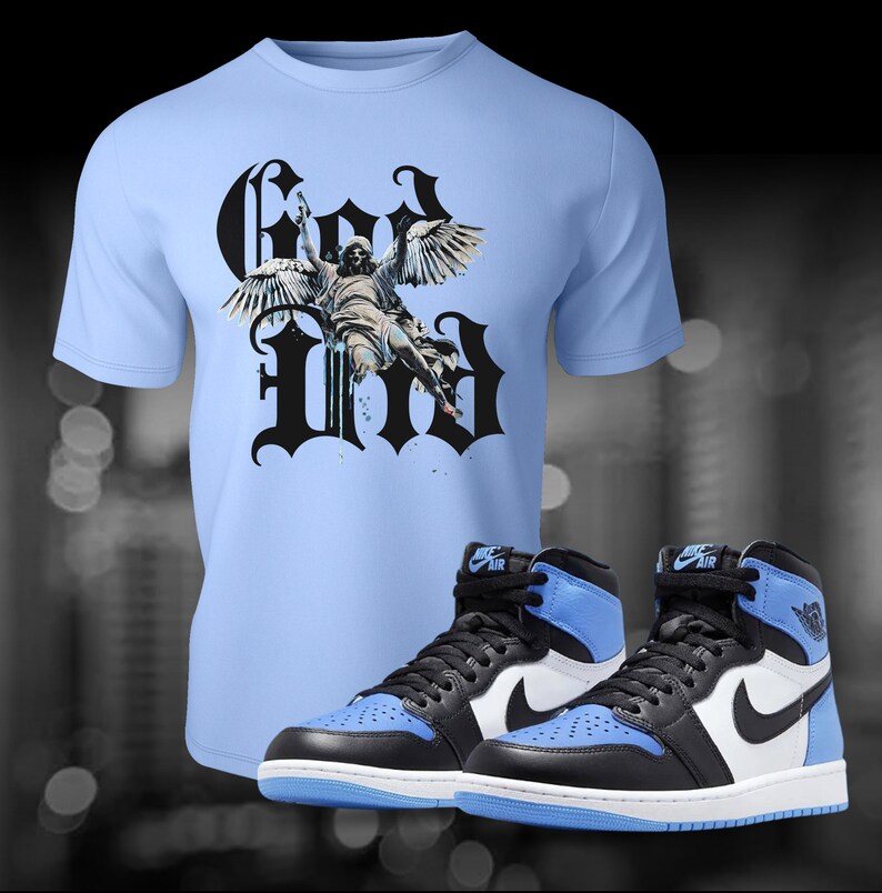 May include: A light blue t-shirt with a black graphic of an angel with wings and the word "God" in black gothic lettering. A pair of black and blue high-top trainers with a white swoosh logo.