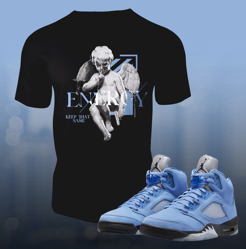 Pu&ograve; includere: Una maglietta nera con una grafica di un cherubino con le ali e il testo "ENERGY KEEP THAT SAME". Un paio di scarpe da ginnastica blu chiaro con accenti neri.