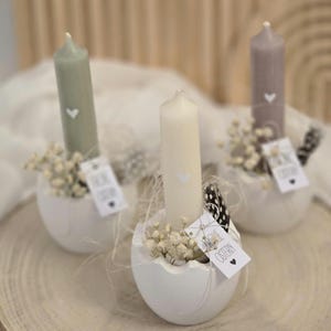 May include: Three white ceramic egg-shaped candle holders with small white candles. Each candle has a small white heart design. The holders are filled with white baby's breath flowers and feathers. One tag reads "Love the  ordinary".