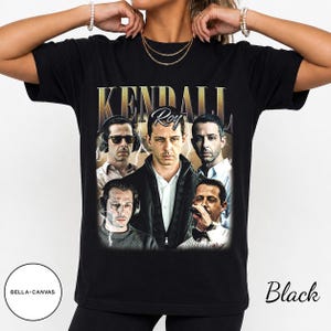 May include: A black t-shirt featuring a graphic print of Kendall Roy from the television series Succession. The design includes the text KENDALL ROY in a bold font, surrounded by five different photographic portraits of the character.
