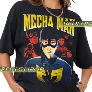 May include: Black t-shirt with the text "MECHA MAN" in yellow block letters. The shirt features a graphic of a character in a blue and yellow uniform with a black mask, surrounded by other masked figures. The brand name "REDLOLIPOP" is visible.