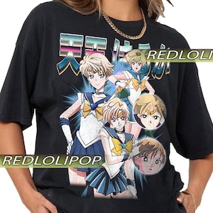 以下が含まれることがあります： セーラー服を着たアニメキャラクターが描かれた黒いTシャツ。デザインには日本語のテキストと「REDLOLIPOP」の文字が含まれています。キャラクターは金髪で、青と黄色のアクセントがあります。シャツはレトロなスタイルです。