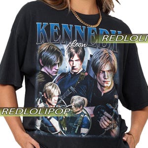 May include: Black t-shirt featuring a graphic of Leon Kennedy from the video game Resident Evil. The design includes the text "KENNEDY" in blue and "Leon" in white, along with multiple images of the character. The shirt has a vintage style.