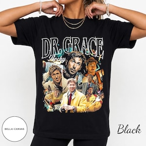 Puede incluir: Una camiseta negra de manga corta con un estampado gráfico que incluye el texto DR. GRACE y Rocky. El diseño muestra varias imágenes fotográficas de un hombre con diferentes atuendos y poses, sobre un fondo oscuro con acentos coloridos.